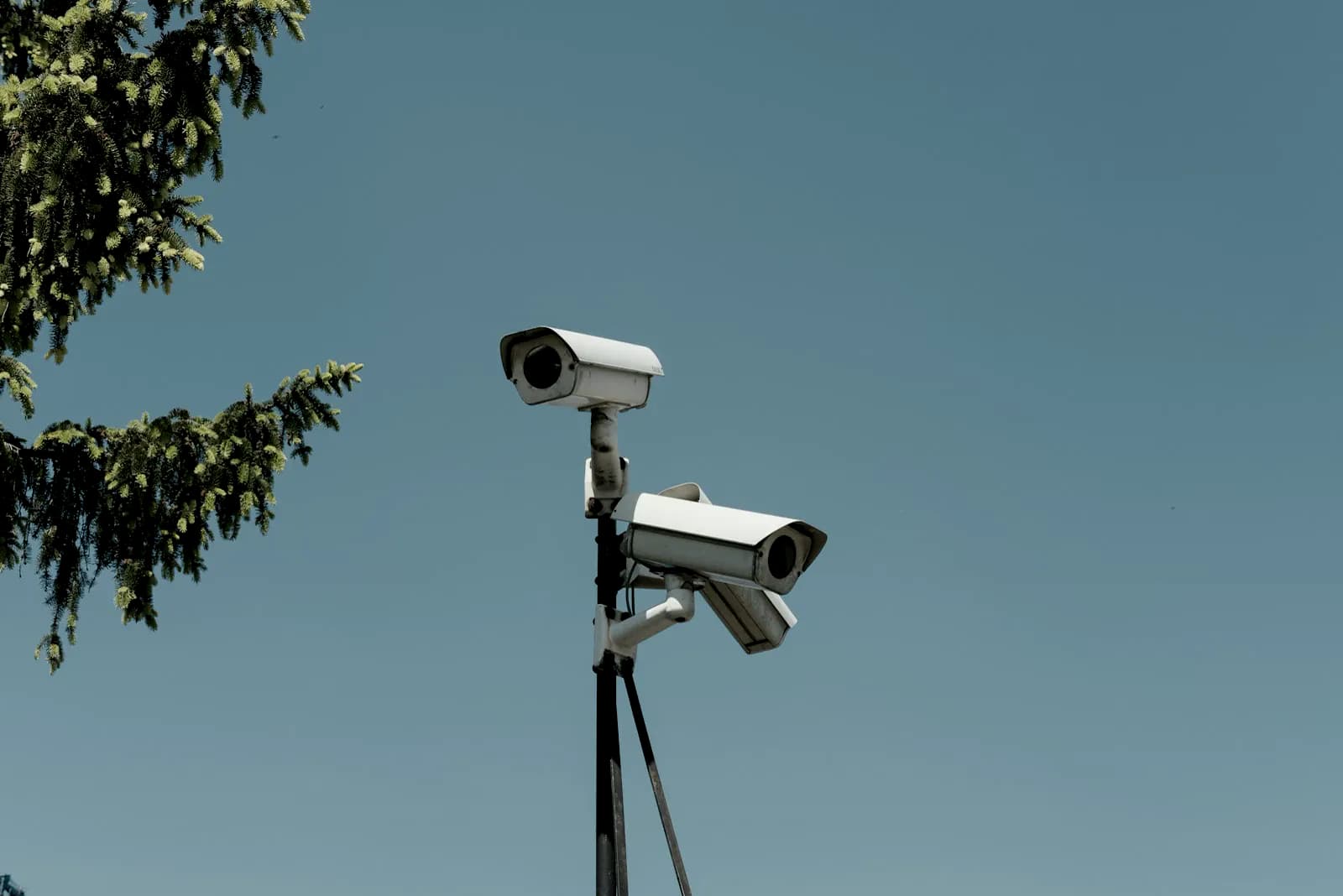 Two surveillance cameras mounted on a pole against a blue sky